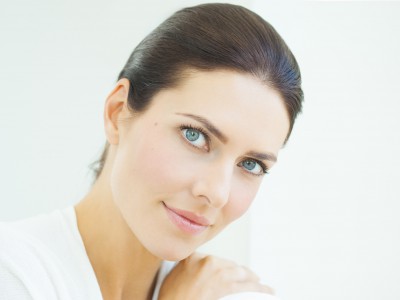 Beautiful natural European woman sitting in daylight at window with serene expresssion. Blue eyes and dark hair.